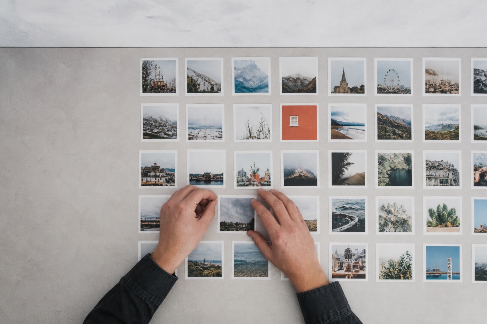 Printed photos laid out in tidy rows on a desk, one being adjusted into place